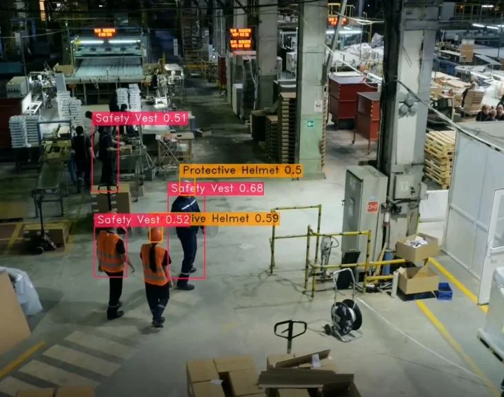 Detections on factory footage — safety vests and protective helmets with confidence scores.